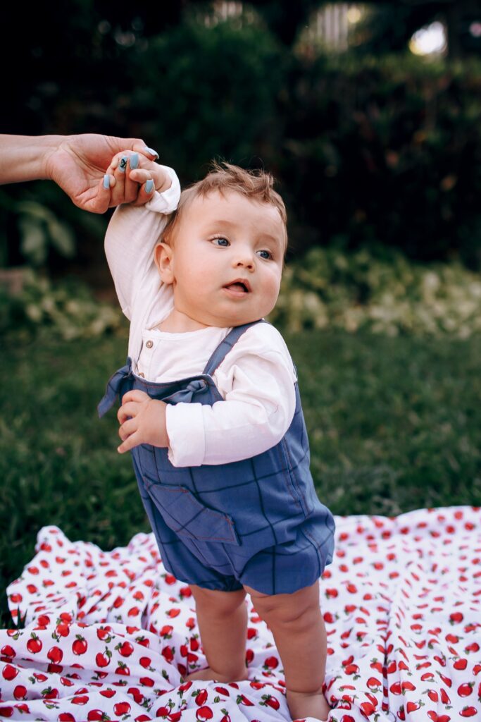 Cute toddler standing on a blanket outdoors, exuding joy and innocence.